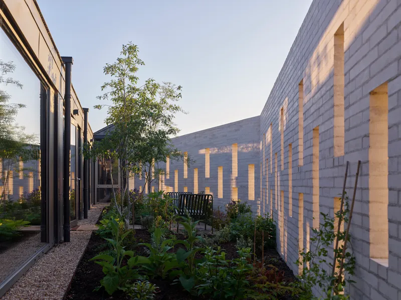 Planted courtyard with illuminated brick wall pattern and young trees at dusk