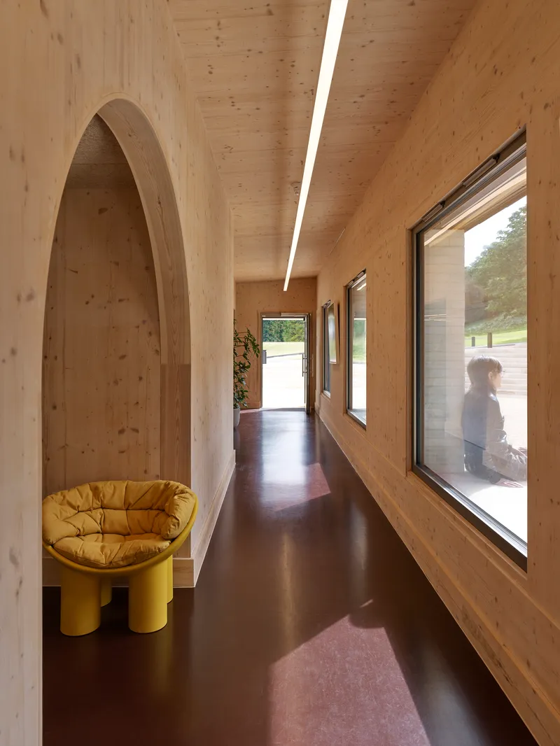 Arched timber corridor with skylight and yellow chair beside a window overlooking a person outside