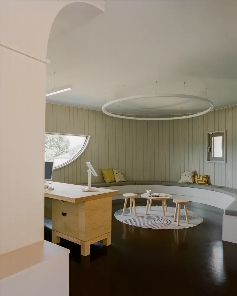 Interior with curved benches against pale timber walls and circular light fixture suspended from vaulted ceiling