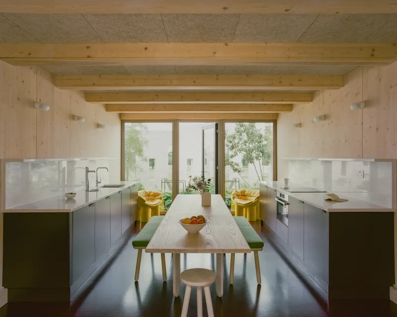 Kitchen with timber ceiling beams and central dining table looking toward glazed doors and planted courtyard