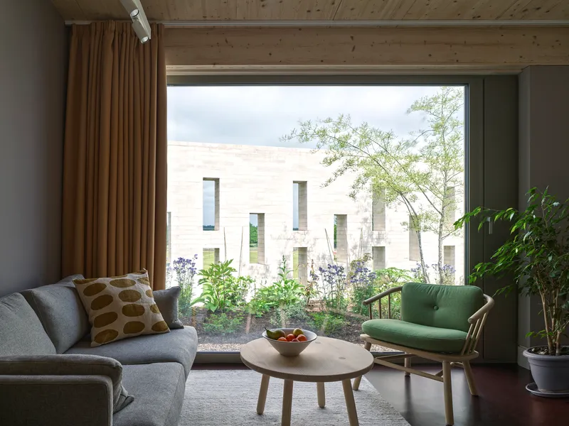 Living room with floor-to-ceiling window opening to a planted courtyard enclosed by pale stone walls