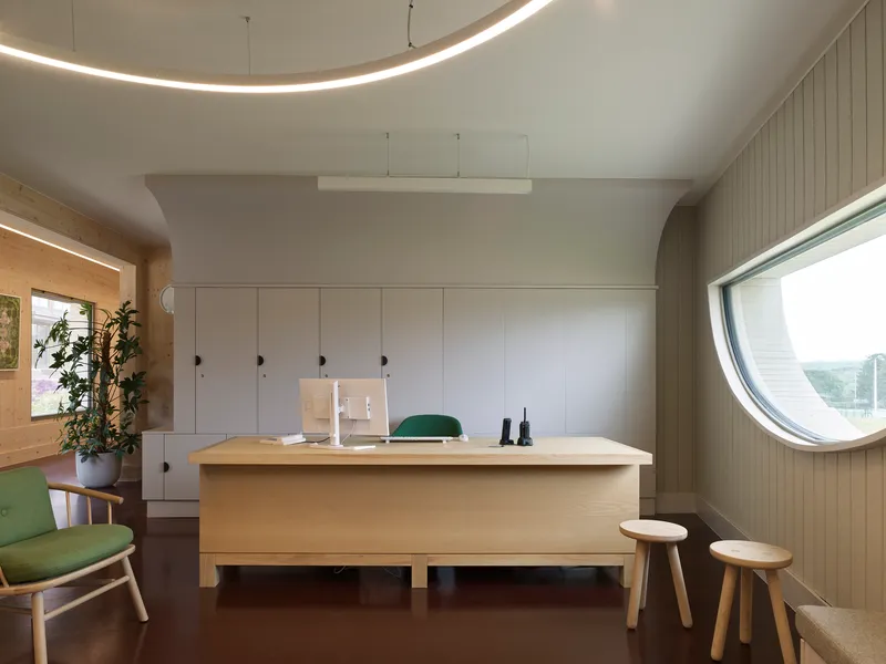 Workspace with circular window and curved ceiling detail lit by recessed linear lighting