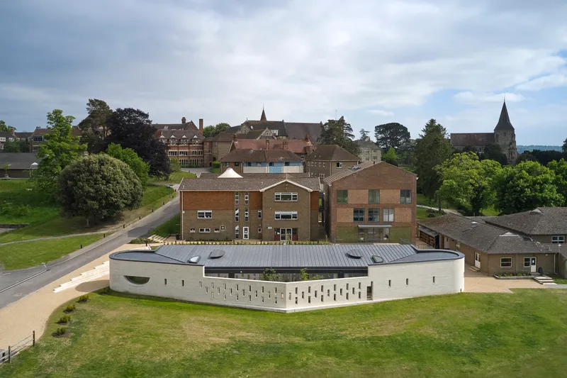 Aerial view of the curved white perforated facade set within a campus of brick buildings