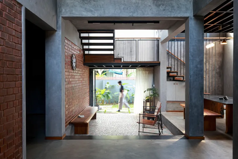 Entry hall with concrete columns and mezzanine bridge framing view to garden with figure walking