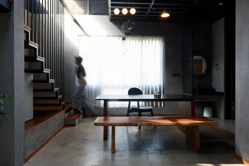 Living space with timber dining table and bench, a figure descending the staircase in motion