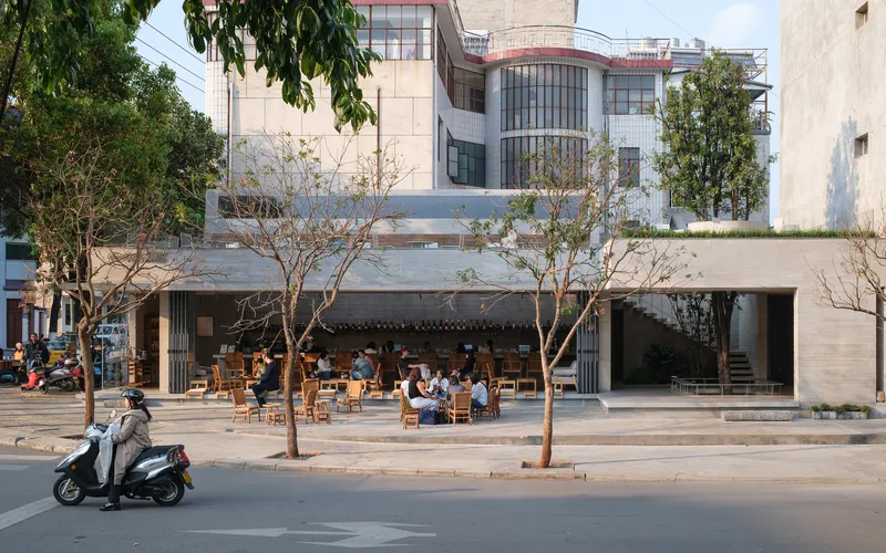 Street view of a cafe with open facade and outdoor seating under street trees with a motorbike passing