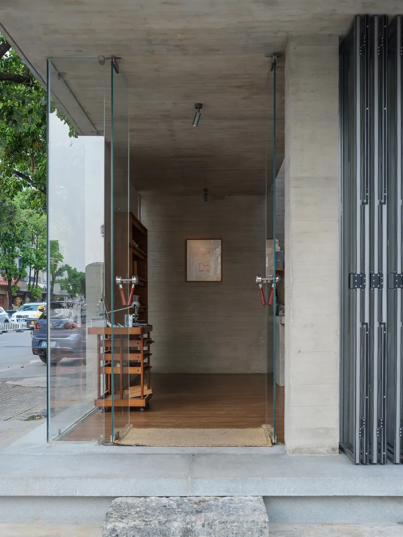 Glass entrance door suspended from board-formed concrete canopy on a wet sidewalk