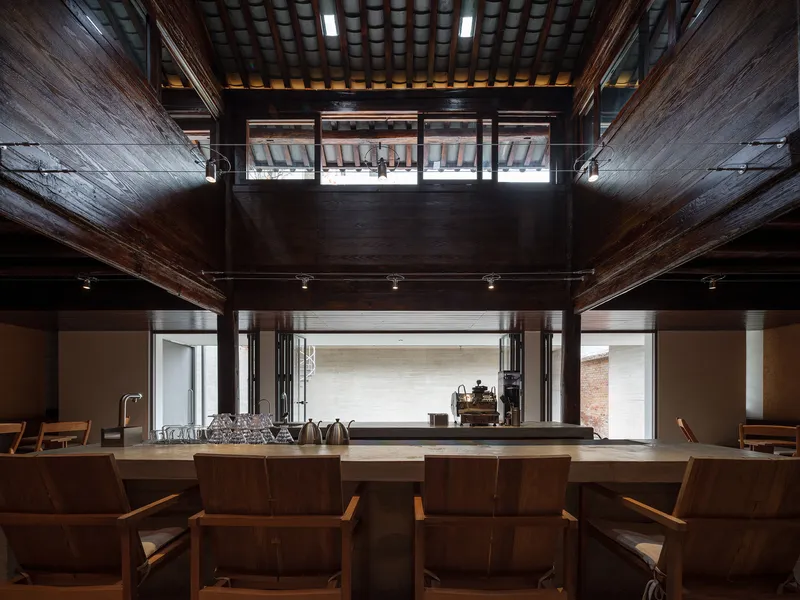 Double-height interior with exposed timber beams and mezzanine overlooking a long counter and wooden seating below