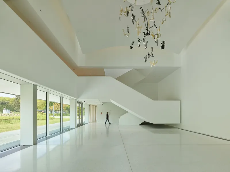 White terrazzo entrance hall with cantilevered stair and a figure crossing beneath a hanging sculpture