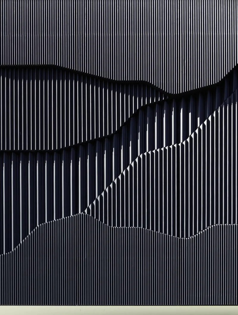 Close-up of vertical metal fin cladding forming wave-like shadows across the facade surface