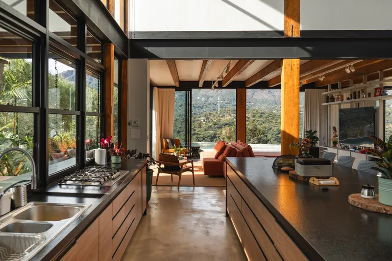 Open kitchen with exposed timber ceiling beams and black steel mezzanine overlooking valley landscape