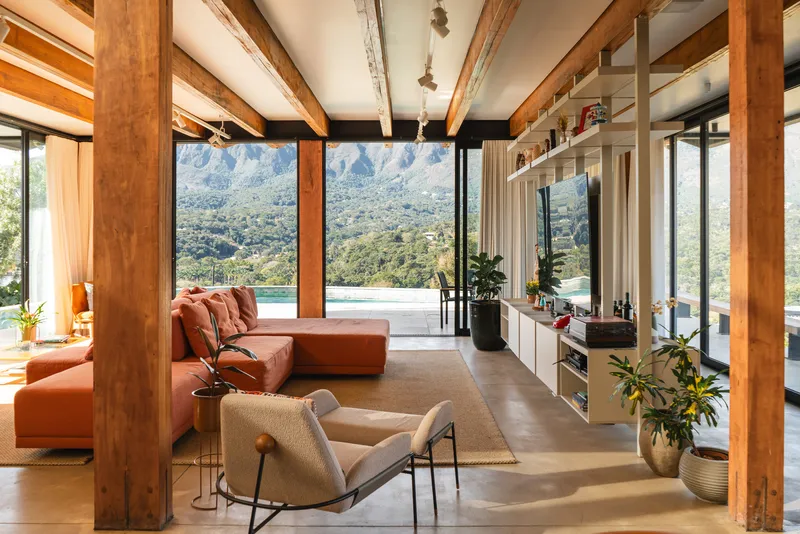 Living area with exposed timber beams and concrete floor opening to terrace with mountain backdrop