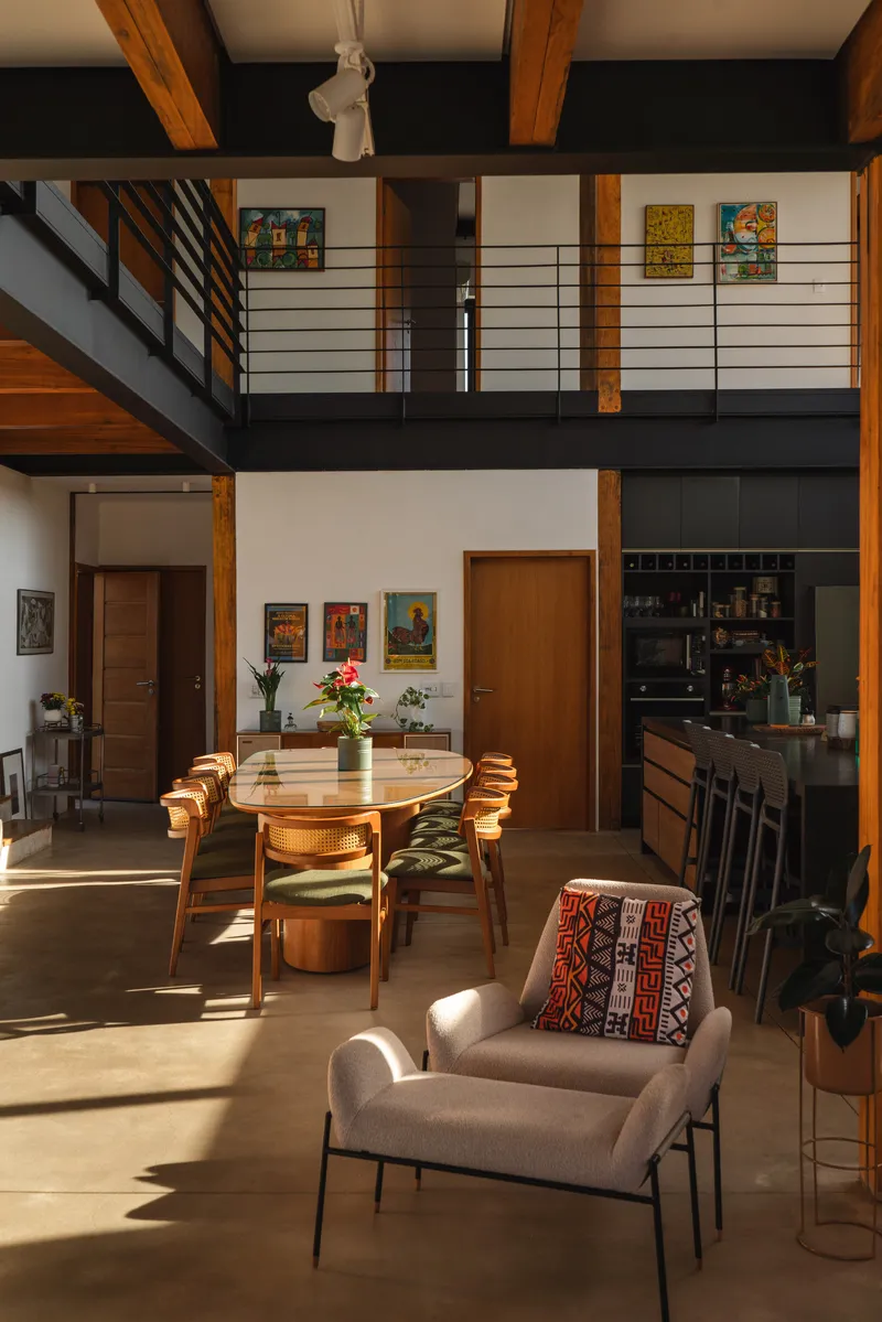 Double-height living space with exposed timber beams, mezzanine balcony and afternoon sunlight on polished floor