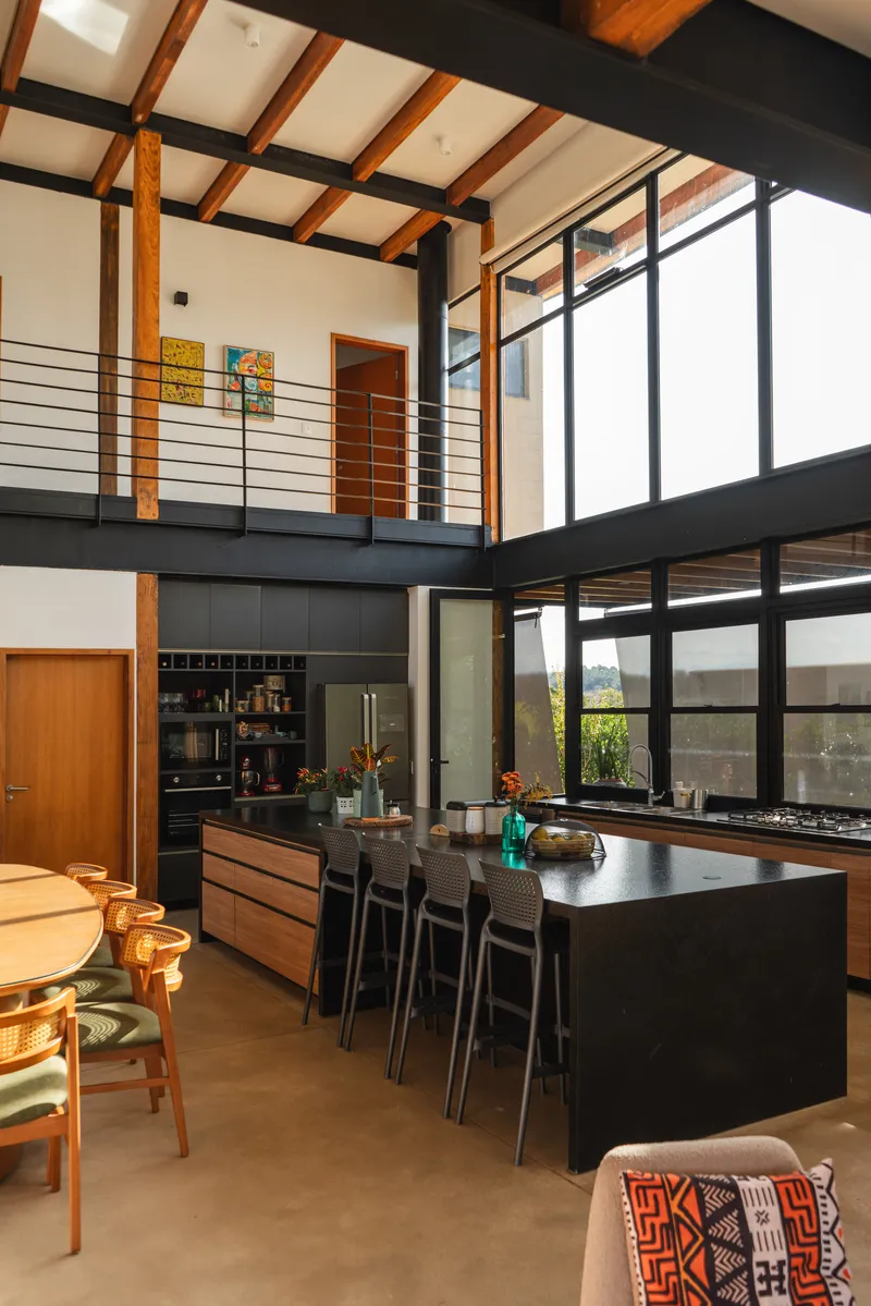 Kitchen island beneath mezzanine level with timber ceiling joists and floor-to-ceiling glazing overlooking planted courtyard