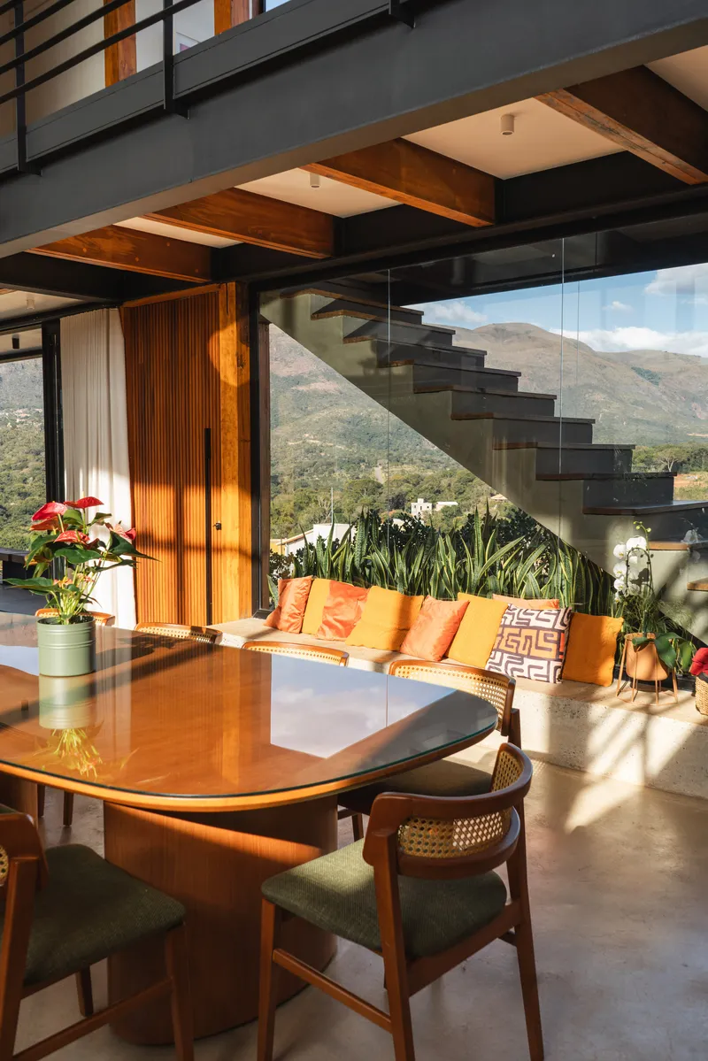 Dining area with floating steel staircase and glass balustrade framing mountain view beyond planted terrace