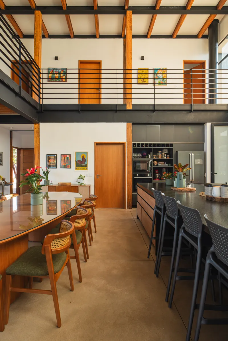 View across dining table toward kitchen island showing mezzanine bridge with horizontal steel railings above