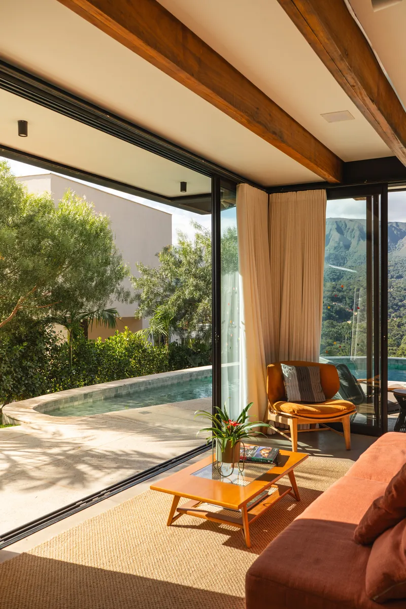 Living room opening to terrace with pool, framed by floor-to-ceiling glass and timber ceiling beams