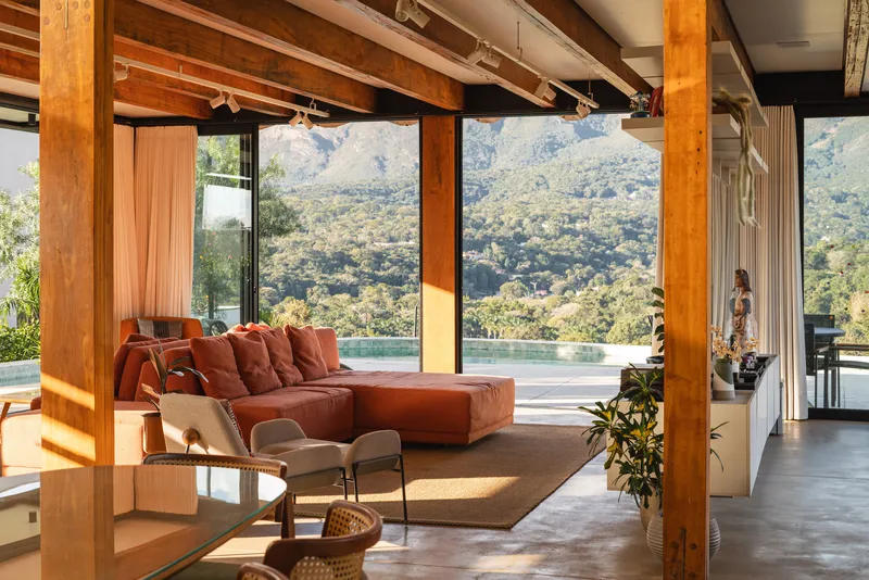Open living area with exposed timber columns and full-height glazing overlooking infinity pool and hillside