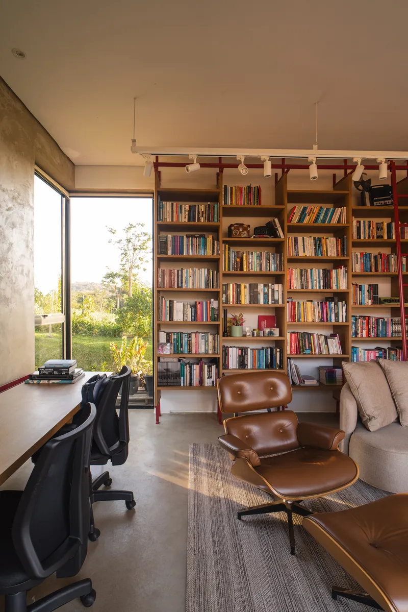 Home office with floor-to-ceiling bookshelves, red steel ladder rail and corner window view