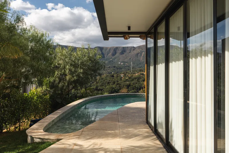 Curved pool terrace with stone pavers beside full-height sliding glass walls and mountain backdrop