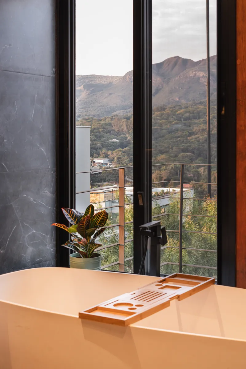 Floor-to-ceiling black-framed glass doors opening to a balcony with distant mountains and afternoon light