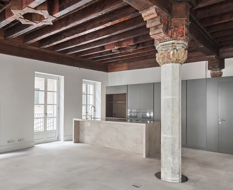 Open kitchen with marble island and grey cabinetry beneath exposed timber beams and an ornamental stone column