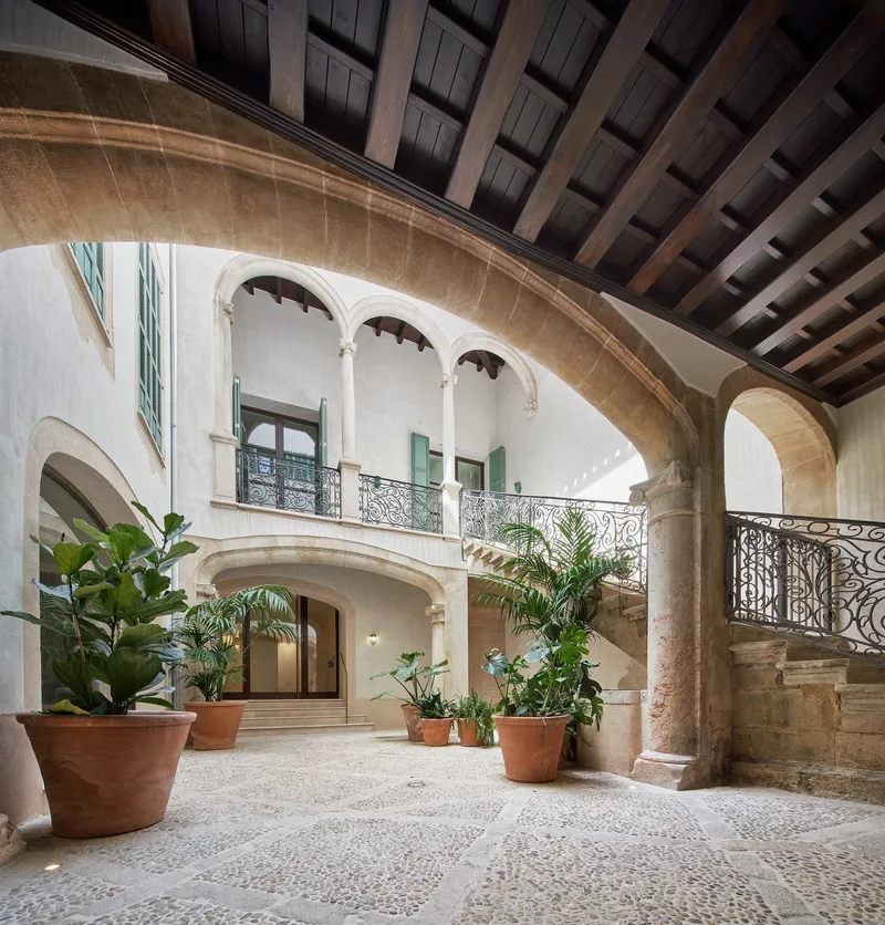 Interior courtyard with pebble mosaic flooring, potted palms and curved stone archway under coffered timber ceiling