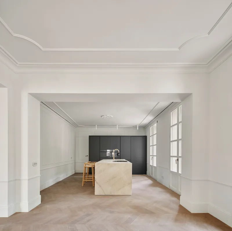 Kitchen with stone island and dark cabinetry framed by white paneled walls and glazed doors