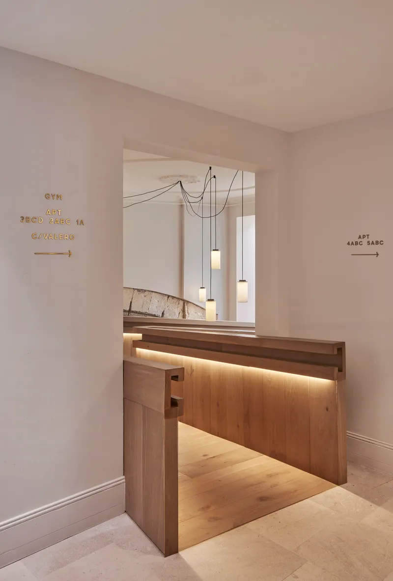 Reception desk of timber with integrated lighting below multi-drop pendant lights and directional signage