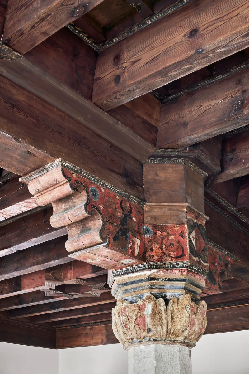 Close-up of painted timber capital with red and blue motifs supporting dark wooden ceiling beams