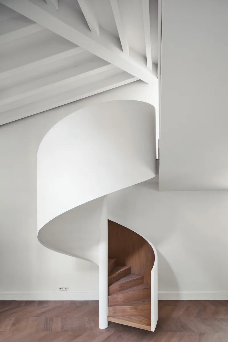 White spiral staircase with timber treads rising through an opening beneath painted wood ceiling joists