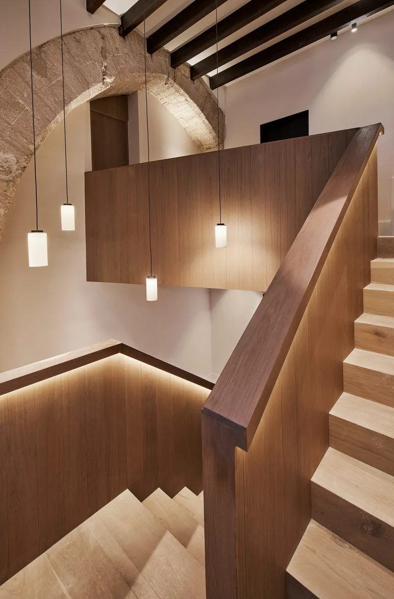 Stairwell with walnut handrail and pendant lights beneath a restored stone arch and timber ceiling beams