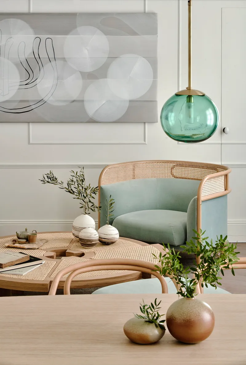 Caned armchair with pale green upholstery beneath a teal glass pendant light and white paneled wall