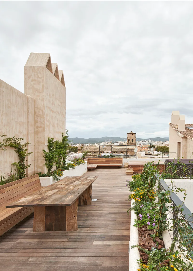 Rooftop terrace with timber decking and planted beds overlooking a bell tower under overcast skies