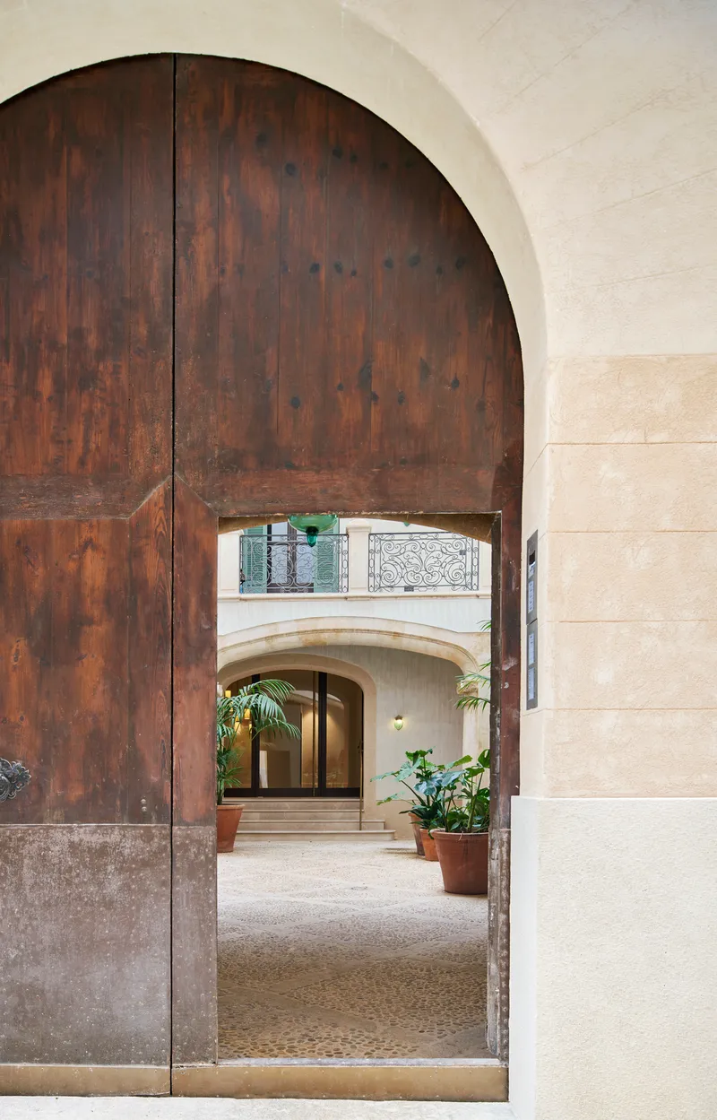 Arched timber door opening into a stone courtyard with potted plants and wrought iron balcony above