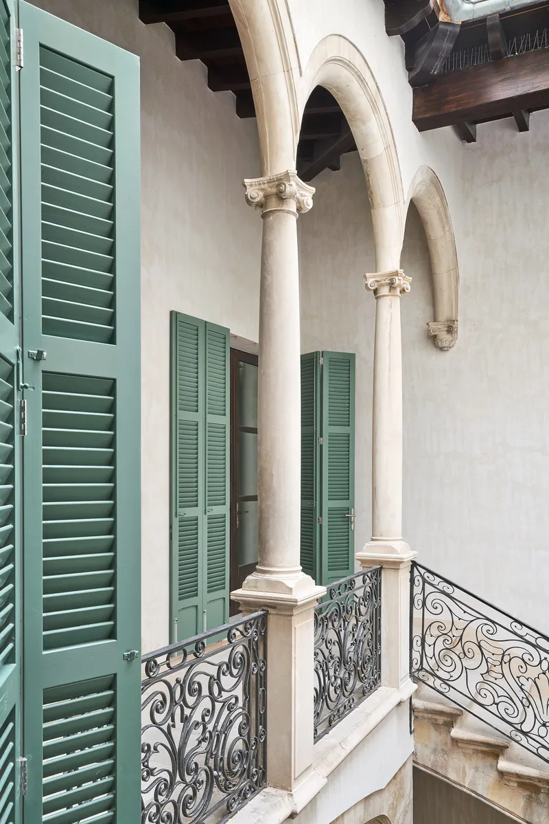 Upper-level courtyard with green louvered shutters, white stucco walls, ornamental iron railings and exposed timber beams