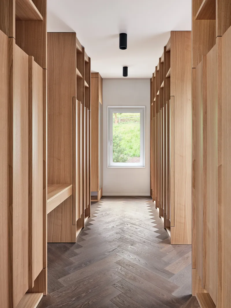 Corridor with chevron wood flooring flanked by timber shelving leading to window with garden view