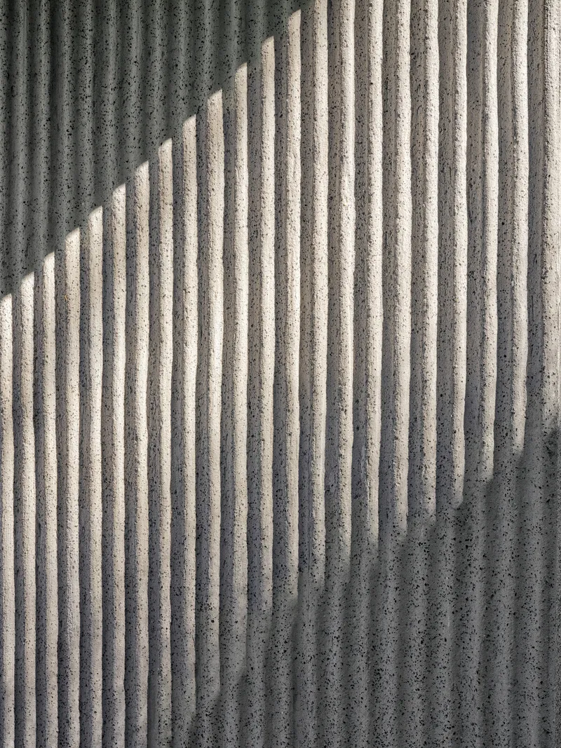 Close-up of ribbed concrete surface with diagonal shadow pattern cast across vertical grooves
