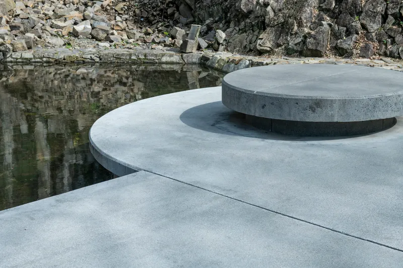 Layered circular concrete platforms beside a reflecting pool with quarried rock wall beyond