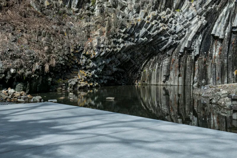 Concrete platform edge meeting a still water pool beneath towering basalt cliff formations