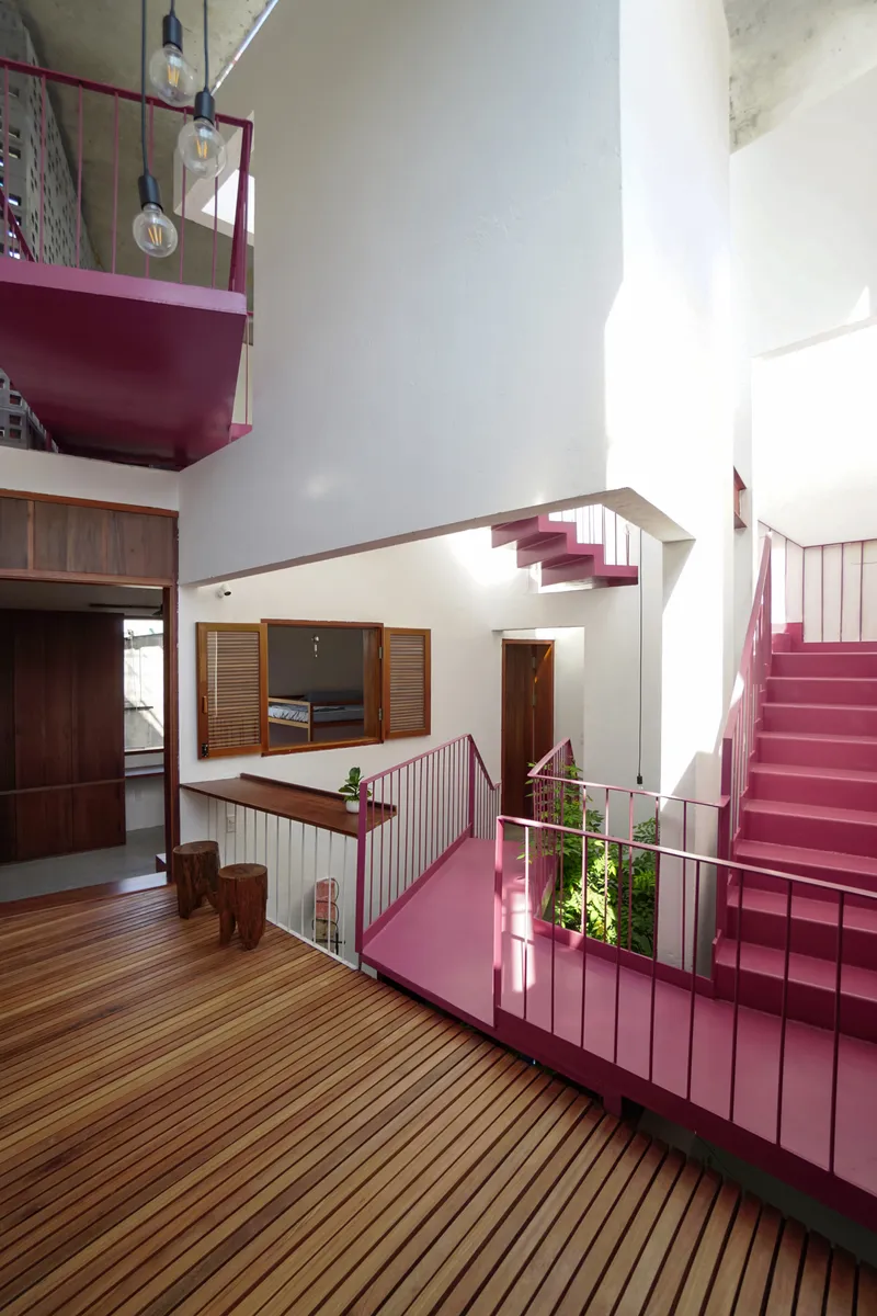 Double-height interior space with pink metal staircases and timber-decked floor under natural daylight
