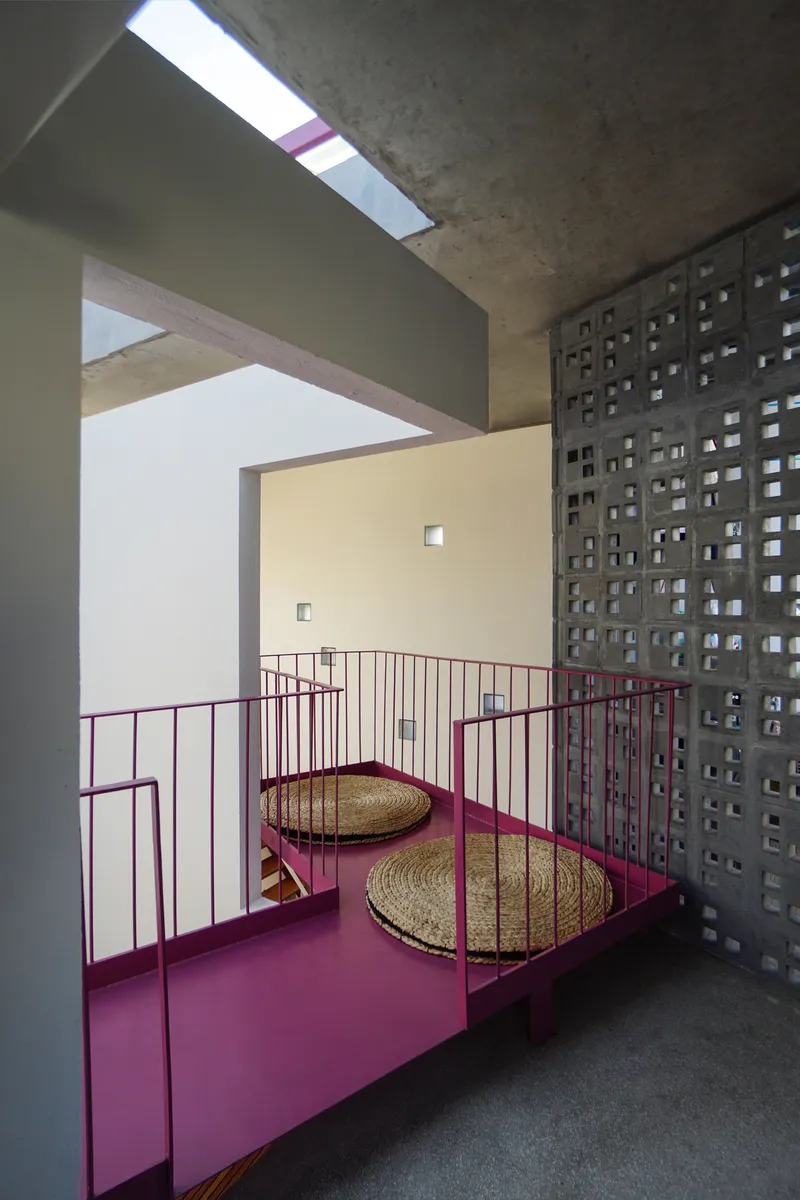 Pink steel landing platform with woven floor cushions beneath a concrete breeze block wall and skylight