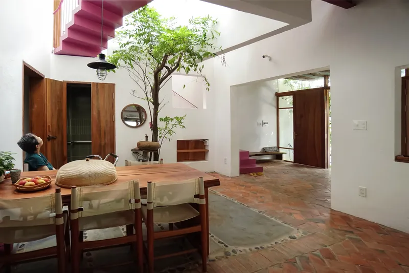 Dining area with terracotta tile flooring and a potted tree beneath suspended pink stair volumes