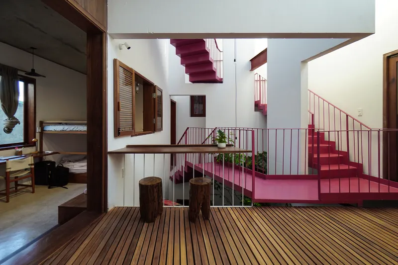 Central void with intersecting pink staircases and timber screen partitions viewed from upper level