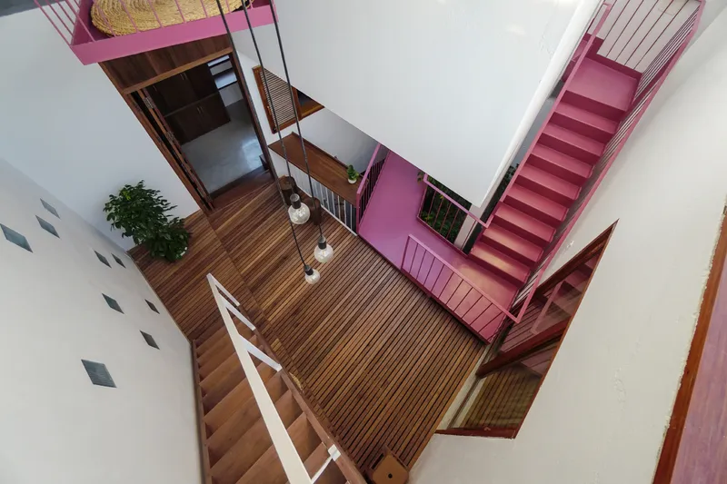 Top-down view of interconnected pink steel staircases around a central void with timber decking