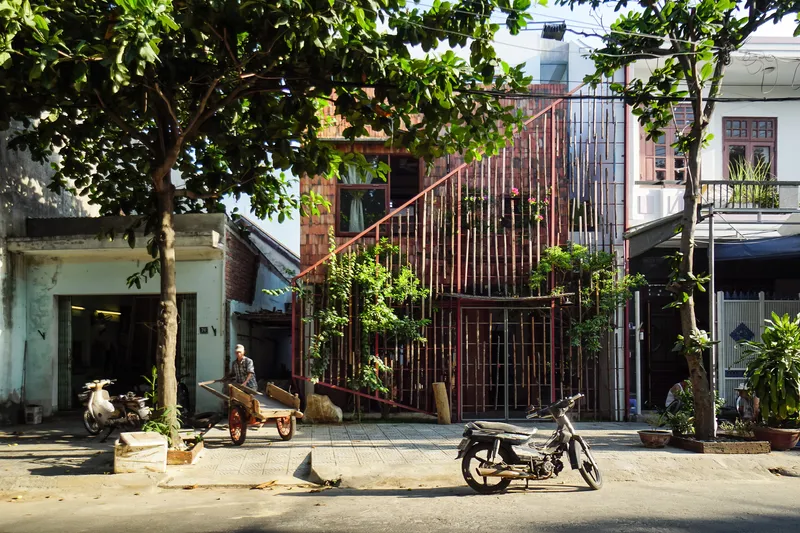 Street view of the vertical metal slat facade with planted vegetation framed by leafy street trees