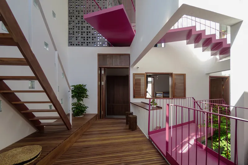 Multi-level interior atrium with timber flooring and pink metal stairs and railings under natural light