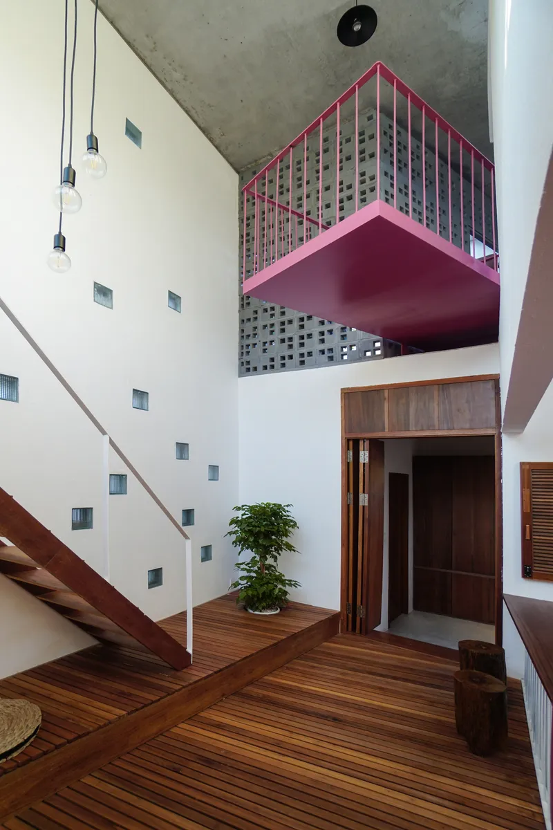 Interior view showing the pink perforated metal balcony suspended above timber floors and diagonal stairs