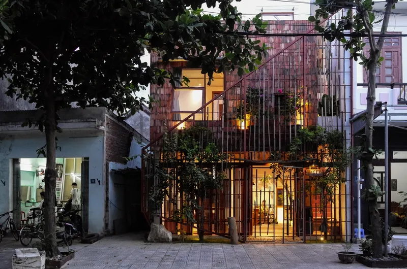 Evening view showing the illuminated interior visible through the metal rod facade and planted terraces