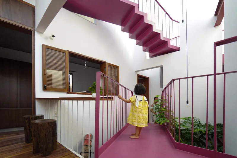 Upper-level walkway with maroon railings and floating staircase above a planted courtyard with a child